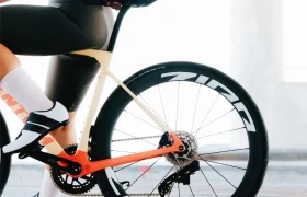 Un ciclista, vestido con un maillot blanco y negro, está sentado en una bicicleta de carretera moderna equipada con ruedas Zipp 404 S, conocidas por su velocidad, en una fotografía tomada de perfil.