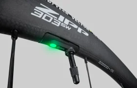 Primer plano de una rueda de bicicleta Zipp 303 de fibra de carbono con una válvula de neumático y un dispositivo que emite una luz verde, que ofrece conectividad inteligente para ayudarte a rodar más rápido.