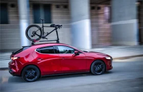Un coche rojo circula por una calle de la ciudad con un portabicicletas Allen Smart Suction Bike Rack sujetando firmemente una bicicleta negra en el techo.