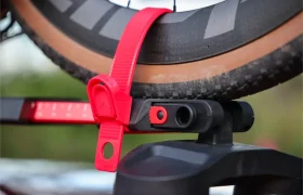 Primer plano de un neumático de bicicleta fijado a un portabicicletas Allen Smart Suction con una correa de plástico roja y un mecanismo de bloqueo.