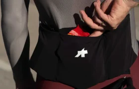 Un ciclista con un maillot ASSOS MILLE GT S11 mete la mano en el bolsillo trasero y saca un gel energético junto a una bicicleta, mostrando la evolución real y el confort inteligente en cada salida.