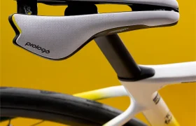 Primer plano de un sillín moderno de bicicleta de color blanco y negro montado en una bicicleta de carretera, con un fondo amarillo.