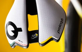 Primer plano de un sillín de bicicleta Prologo blanco con el logotipo del Tour de Francia y detalles en negro, amarillo y rojo, sobre un fondo amarillo.
