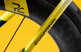 Primer plano de una rueda de bicicleta y un cuadro con detalles en amarillo y el logotipo «COUNTERVAIL», sobre un fondo amarillo liso.