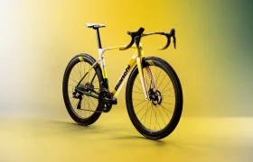 En un fondo amarillo degradado se muestra una bicicleta de carretera Bianchi de color amarillo y blanco, con manillar de carretera y frenos de disco.
