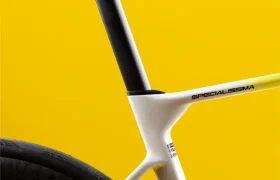 Primer plano del sillín, la tija del sillín y la rueda trasera de una bicicleta de carretera moderna sobre un fondo amarillo brillante.
