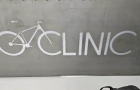 Un cartel con la palabra "Biciclinic", donde la letra "C" está estilizada como el diseño de una rueda y un cuadro de bicicleta, se destaca sobre un fondo gris.