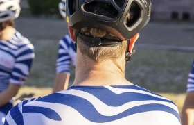 Un grupo de ciclistas que llevan maillots a juego azules y blancos y cascos negros se encuentra reunido al aire libre, visto desde atrás.