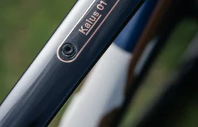 Primer plano de un cuadro de bicicleta BMC Kaius 01 con una placa metálica con la inscripción "Kailus 01", que destaca esta bicicleta rápida en medio de un fondo borroso.