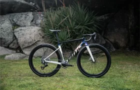 Una BMC Kaius 01 bicicleta rápida negra, blanca y azul está aparcada sobre hierba delante de rocas y plantas verdes al aire libre.