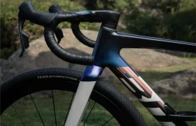 Primer plano de una BMC Kaius 01, una bicicleta rápida, destacando el manillar, la rueda delantera y parte del cuadro, en exteriores con rocas y vegetación de fondo.
