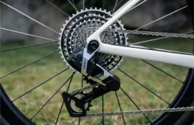 Primer plano de la rueda trasera de una bicicleta BMC Kaius 01 que muestra un casete, una cadena y un desviador SRAM sobre un fondo cubierto de hierba, perfecto para los que quieren rodar rápido.