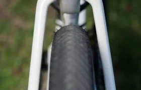 Primer plano del neumático trasero y el cuadro blanco de una BMC Kaius 01, mostrando la holgura del neumático de esta bicicleta rápida sobre un fondo de hierba.