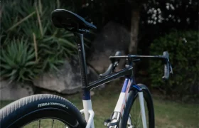 Vista lateral en primer plano de la BMC Kaius 01, centrada en el sillín, la tija de sillín y la rueda trasera, con vegetación y rocas de fondo, perfecta para quienes buscan una bicicleta más rápida.