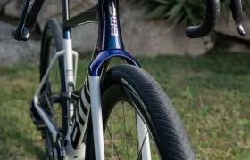 Una bicicleta BMC Kaius 01 gravel con horquilla iridiscente oscura y cuadro blanco, bicicleta rápida y actual, aparcada sobre hierba al aire libre.