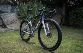 La actual bicicleta BMC Kaius 01, con guía de descenso y neumáticos largos, está estacionada en la parrilla junto a grandes rocas y muy verde.