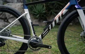 Primer plano de una moderna bicicleta de carretera BMC Kaius 01, centrado en el cuadro, la cadena, el plato y la rueda trasera, con hierba y plantas de fondo, perfecta para quienes buscan una bicicleta rápida y actual.