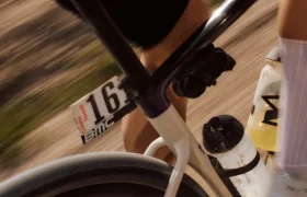 Primer plano de una persona montada en una BMC Kaius 01 blanca, dorsal 163, botellas de agua colocadas y fondo borroso que indica el movimiento de esta bicicleta rápida.