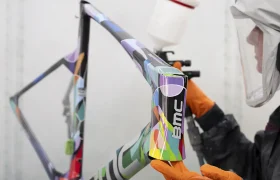 Una persona que usa equipo de protección pinta con aerosol un colorido cuadro de bicicleta BMC VAR0 en un taller.