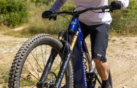Una persona que lleva casco y gafas de sol sube en bicicleta de montaña por un sendero de tierra rodeado de vegetación bajo un cielo despejado, disfrutando de más potencia y más control gracias al Bosch Performance Upgrade.