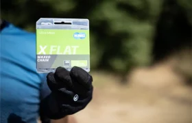 Una persona con un guante negro sostiene un paquete de cadena KMC X Flat al aire libre, mostrando la duradera cadena encerada para bicicletas.