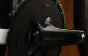 Primer plano de un plato de bicicleta con un brazo de biela Shimano Ultegra, un plato de fibra de carbono Aurora Green y una cadena KMC X12L Waxed para una cadena eficiente.