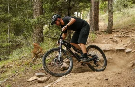 Una persona vestida con ropa de ciclismo negra va en bicicleta de montaña, equipada con cubiertas Continental Gravity para MTB, por un sendero de tierra en una zona boscosa, levantando polvo y esquivando rocas y raíces de árboles mientras explora nuevas combinaciones en un terreno exigente.