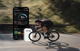 Un ciclista circula por una carretera mientras la pantalla de un smartphone muestra datos sobre su rendimiento en bicicleta y en primer plano se ve un sensor CORE.