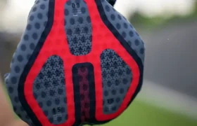 Una mano sostiene un guante de ciclismo acolchado, de color gris y rojo, con una empuñadura texturizada con motivos de estrellas, al aire libre, con la hierba difuminada al fondo; perfecto para combinarlo con el conjunto Castelli Climber’s A/C y mejorar el rendimiento térmico en las salidas en días cálidos.