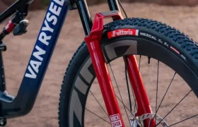 Bicicleta de montaña Van Rysel con cuadro azul, horquilla delantera RockShox roja y neumáticos con tacos.