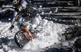 Un ciclista atraviesa una espesa capa de nieve con una bicicleta de montaña, haciendo que la nieve salpique alrededor de las ruedas, como si en una entrevista Jordi Bagó hablara de actividades aventureras.
