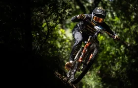 Un ciclista de montaña a toda marcha baja rápidamente por una pista forestal, rodeado de árboles y de la luz del sol moteada, que recuerda el espíritu aventurero que se ve en una entrevista Jordi Bagó.