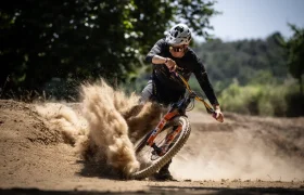 Un ciclista con casco hace un giro brusco en un camino de tierra, lo que hace que se levante una nube de polvo detrás de la bicicleta, que recuerda escenas descritas en una entrevista Jordi Bagó.