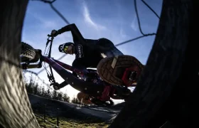 Un ciclista con casco se inclina bruscamente sobre una bicicleta de montaña durante un giro, visto desde un ángulo bajo con el cielo de fondo, captando una acción que recuerda a una foto de entrevista al estilo Jordi Bagó.