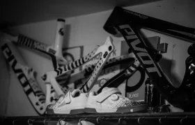 Tres cuadros de bicicleta están montados en una pared encima de una estantería que contiene zapatillas de ciclismo; la imagen en blanco y negro evoca el estilo minimalista admirado a menudo por jordi bagó.