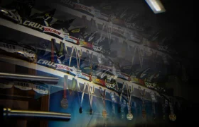 Un expositor de medallas y dorsales colgaba de una pared, con estantes que sostenían trofeos y placas de identificación de la marca Santa Cruz sobre ellos, recordando escenas de una entrevista Jordi Bagó.