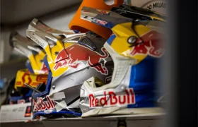 Varios cascos de motocicleta con la marca Red Bull están alineados en un estante, con colores azul, amarillo y plata y destacados logotipos de Red Bull, perfectos para cualquier aficionado después de ver la entrevista a Josep García.