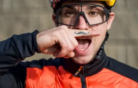 Un hombre con casco de moto y gafas sostiene un objeto en forma de bigote bajo la nariz, con la boca abierta, vestido con una chaqueta naranja de KTM durante una entrevista a Josep García.