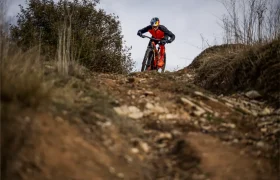 Un ciclista de montaña vestido de rojo y negro desciende por un sendero pedregoso de tierra rodeado de hierba seca y arbustos, que recuerda el accidentado terreno comentado en la entrevista a Josep García.