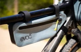 Primer plano de una bolsa para cuadro EVOC de color gris claro, esencial para EVOC Bikepacking, fijada al tubo superior y al tubo inferior de una bicicleta con correas negras de velcro para una mayor protección de la bicicleta.