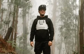 Un hombre vestido con ropa de ciclismo y un protector de torso EVOC (talla XS) se encuentra en un camino de tierra en un bosque neblinoso, rodeado de altos árboles y denso follaje, dando prioridad a la seguridad mientras explora la naturaleza salvaje.