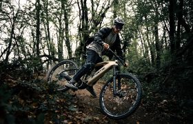 Una persona conduce una Fantic Sierra e-MTB con motor Bosch CX Gen5 por un sendero de tierra a través de un bosque denso y verde, inclinándose en una curva.