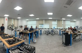 Un grupo de personas trabaja en el montaje de bicicletas en mesas separadas en un amplio y luminoso taller equipado con herramientas y piezas de bicicleta, participando en Formaciones Shimano 2026.