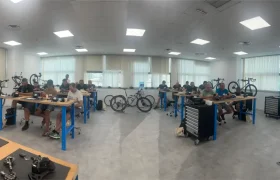 Durante una de las sesiones de Formaciones Shimano 2026, varias personas están sentadas en bancos de trabajo en un luminoso taller, montando o reparando bicicletas con diversas piezas y herramientas visibles por toda la sala.