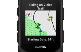 Un ciclocomputador Garmin Edge MTB muestra un mapa de senderos con el mensaje "Riding on Violet Trail" y "Starting Gate: 61 ft" en la pantalla.
