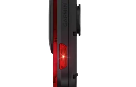 Vista lateral de una luz trasera de ciclismo Garmin Varia RearVue 820 negra con lente iluminada en rojo, aislada sobre fondo blanco.