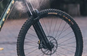 Una mano rocía el producto de limpieza sin agua «Grit» sobre el cuadro delantero y la horquilla de una bicicleta de montaña.