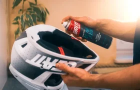 Unas manos rociando limpiador en espuma en el interior de un casco de moto blanco.