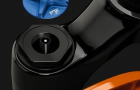 Primer plano de una horquilla de suspensión FOX 38 2027 Enduro que muestra un mando de ajuste FOX Float azul, destacando el control preciso y los elegantes componentes negros y naranjas sobre un fondo oscuro.
