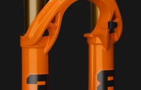 Primer plano de una horquilla de suspensión FOX 38 2027 de color naranja para una bicicleta, con números negros y dos tubos de montante dorados, diseñada para la práctica del Enduro, sobre un elegante fondo negro.